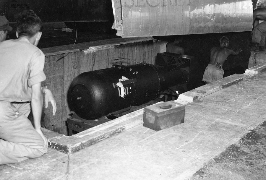 This picture shows two men standing around the bomb as they prepare to load it into the airplane for delivery.